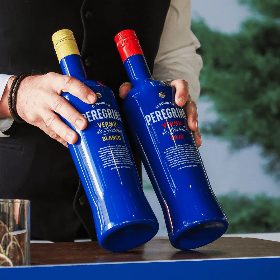 Manos que sostienen dos botellas azules de Vermú Peregrino